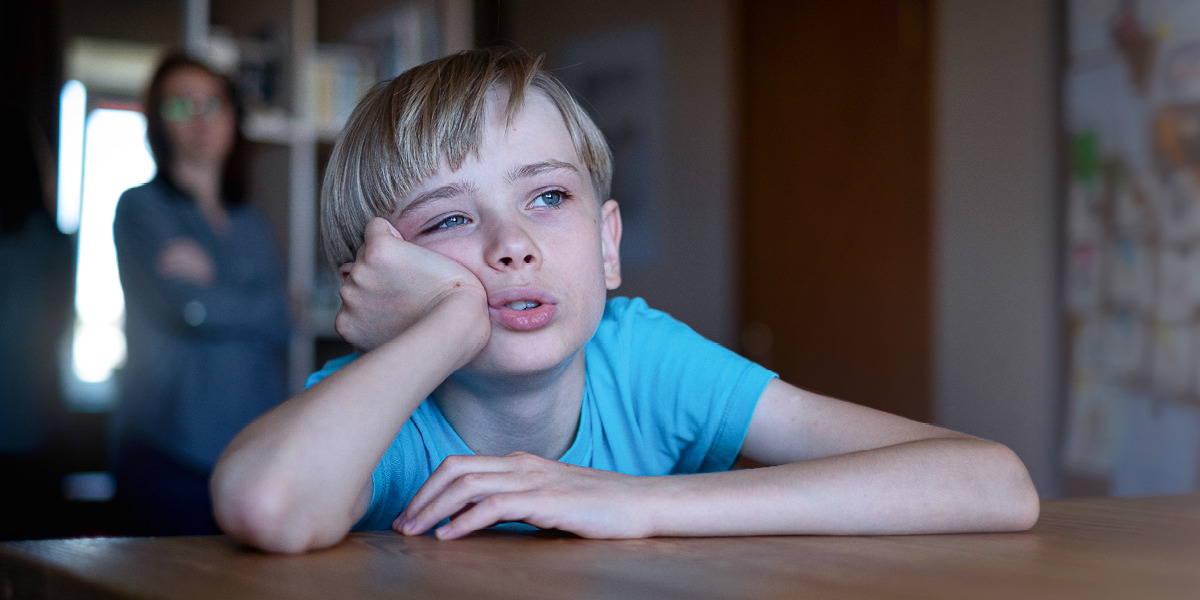 Znuděné dítě sedí u stolu s rukou pod bradou